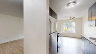 Located in Portland, OR, this single-floor, 2-bedroom, 1-bathroom unit offers a practical and well-organized layout. The combined kitchen and living area forms the heart of the home, featuring light wood-style flooring throughout. The kitchen is equipped with dark cabinetry and ample storage in one configuration, while another variation showcases sleek grey cabinetry with white countertops, a stainless steel range, and a ceiling fan overhead. A large window and sliding glass door flood the living area with natural light and provide direct access to a private balcony overlooking lush greenery. The spacious primary bedroom features plush grey carpeting, a wide window with outdoor views, and a baseboard heater. The second bedroom also features carpet and a sliding-door closet, offering practical storage. A connecting hallway links the bedrooms to the shared full bathroom, which includes a vanity with dark wood cabinetry, wood-style tile flooring, and grab bars for accessibility. Throughout the unit, clean white walls and neutral tones create a bright, cohesive atmosphere well-suited for comfortable everyday living.