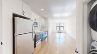 This thoughtfully designed 2-bedroom, 2-bathroom residence offers a clean, modern aesthetic across a single floor. Light-toned hardwood flooring runs throughout, creating a seamless and cohesive feel from room to room. The open-concept layout connects the kitchen directly to the living area, maximizing the sense of space and encouraging easy flow between the two zones. The kitchen is a standout feature, showcasing a two-tone design with crisp white upper cabinetry contrasted by dark navy lower cabinets, all complemented by white countertops, a matte black faucet, and a full suite of stainless steel appliances including a refrigerator, electric range, over-the-range microwave, and dishwasher. Recessed lighting illuminates the kitchen and living area, adding a polished finish. The living room benefits from a large window that invites natural light and outdoor views. Both bedrooms are bright and well-proportioned, with the primary bedroom offering generous dimensions and access to a dedicated closet fitted with wire shelving for organized storage. The bathrooms are finished in a clean, minimalist style with white vanities featuring shaker-style cabinetry and matte black hardware. White walls throughout the residence contribute to a fresh, contemporary ambiance.