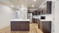 This well-appointed single-floor residence showcases a cohesive modern design carried consistently throughout every room. The kitchen serves as a standout centerpiece, featuring rich dark wood cabinetry with sleek bar-pull hardware, crisp white quartz countertops, and a full suite of stainless steel appliances including a refrigerator, range, and built-in microwave. A large central island with an undermount sink and stylish pendant lighting above creates an ideal space for both meal preparation and casual dining. Light-toned hardwood flooring flows seamlessly from the kitchen into the living areas, enhancing the bright, airy atmosphere created by recessed lighting and natural light from windows fitted with horizontal blinds. The living space is generously proportioned with clean white walls and a neutral palette that lends itself well to a variety of interior styles. Multiple bedrooms offer comfortable, well-lit retreats, each with windows that bring in natural light. The two bathrooms maintain the same design language found throughout, with wood-toned vanities, white quartz countertops, large mirrors, and hardwood-style flooring. One bathroom features a full soaking tub with shower, while the second serves as a well-equipped half or three-quarter bath. The overall aesthetic is clean, contemporary, and move-in ready.