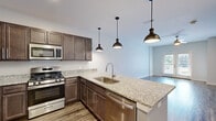 Located at 260 Jr Achievement Dr in Elkhart, Indiana, this single-floor unit offers a thoughtfully designed layout with contemporary finishes throughout. The kitchen serves as a central highlight, showcasing rich dark-toned cabinetry paired with speckled granite countertops that extend across an open peninsula. A suite of stainless steel appliances—including a gas range, built-in microwave, refrigerator, and dishwasher—equips the space for everyday functionality. Three industrial-style pendant lights hang above the peninsula, adding a modern aesthetic touch. Wood-style luxury vinyl plank flooring runs through the main living areas, lending warmth and durability, while French doors in the living area invite natural light and provide outdoor access.

The bedrooms feature plush carpeting and ceiling fans, creating a comfortable retreat. One bedroom includes a walk-in closet with built-in shelving, offering generous storage. The bathroom is finished with a granite-top vanity, dark wood cabinetry, wood-look flooring, and a glass-enclosed walk-in shower. Neutral gray wall tones are consistent throughout, complementing the modern finishes and contributing to a clean, cohesive ambiance across the entire unit.