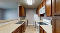 This two-story home is designed with a practical and comfortable layout across both levels. The galley-style kitchen is efficiently arranged with warm medium-toned wood cabinetry lining both walls, offering generous upper and lower storage. Light-toned countertops provide ample prep space, and white appliances — including an electric range, over-the-range microwave, refrigerator, and dishwasher — are included. Stone-look tile flooring runs through the kitchen and extends into the connecting hallway, which features soft gray walls and clean white trim, guiding residents through the home's interior.

The bedrooms are carpeted in neutral tones and each include ceiling fans with integrated lighting. Natural light enters through blinds-fitted windows, and one room features a vaulted ceiling with a built-in desk ledge, adding a functional touch. The bathrooms are finished with stone-look tile flooring, wood vanities with light countertops, and full tub-shower combinations. One bathroom includes a more spacious layout with a separate water closet. Throughout the home, a consistent gray-toned color palette and white trim create a clean, cohesive aesthetic.