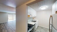 Located on East Camelback Road in Phoenix, Arizona, this single-story unit offers a practical and well-appointed layout throughout. The kitchen is a functional highlight, featuring white cabinetry with brushed nickel hardware, light stone countertops, a double stainless steel sink, an electric range, a dishwasher, and a decorative mosaic tile backsplash that adds visual interest. A range hood and ample upper cabinet storage complete the space.

The living area is finished with wood-style plank flooring and a textured ceiling, and opens directly to an outdoor patio through a sliding glass door dressed with vertical blinds, allowing for natural light and outdoor access. The bedroom is carpeted for comfort and includes a ceiling fan with a light fixture, a window for natural light, and a textured ceiling.

The bathroom is notably spacious, featuring a long double-sink vanity with white cabinetry, a large mirror, and brushed nickel fixtures. A separate wet area includes a full soaking tub and shower combination with white tile surround and coordinating brushed nickel hardware. Wood-style flooring runs through the bathroom and hallway, tying the unit together with a cohesive, clean aesthetic throughout.