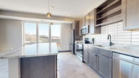 This thoughtfully designed single-floor unit offers a well-appointed layout across a comfortable footprint. The open-concept kitchen and living area serves as the heart of the space, featuring large-format tile flooring, a central island with light granite countertops, and dark wood cabinetry with open shelving. Stainless steel appliances, including a refrigerator, electric range, microwave, and dishwasher, are complemented by a classic subway tile backsplash. Pendant lighting and oversized windows flood the kitchen and living area with abundant natural light while framing outdoor views of the surrounding neighborhood.

The bedrooms are carpeted and offer a calm, neutral palette with large windows that provide additional outdoor views and natural light. Each room includes closet storage with wire shelving, and the dark-framed interior doors add a modern accent throughout. The bathroom is finished with large-format tile flooring, a single vanity topped with granite, an illuminated mirror, and matte black fixtures. A hallway connects the rooms efficiently, with HVAC vents integrated discreetly into the ceiling. Overall, the unit presents a clean, contemporary aesthetic with consistent finishes throughout.