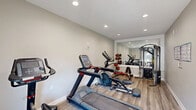 Located in East Ridge, Tennessee, this dedicated fitness center offers a well-equipped exercise space designed to support a comprehensive workout routine. The room features light-toned hardwood-style flooring, neutral gray walls, and recessed lighting that creates a clean, bright atmosphere conducive to focused training.

The space is thoughtfully organized to maximize functionality. Cardio equipment includes a Star Trac treadmill, an elliptical trainer, and a stationary bike, providing a range of aerobic options. A multi-functional cable machine anchors the strength-training area, accompanied by TRX suspension straps for bodyweight training. A dumbbell rack stocked with varying weights, medicine balls, and a flat workout bench round out the free weights section.

A large wall mirror visually expands the room while allowing users to monitor their form during exercise. The motivational wall decal "No Pain, No Gain" reinforces the fitness-focused atmosphere. A glass-paneled exterior door allows natural light to filter in and provides direct outdoor access. A built-in open shelving nook offers additional storage space. An HVAC vent ensures comfortable climate control throughout workouts. The overall design is clean, modern, and purpose-built, making this fitness center a practical and inviting amenity.