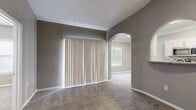 This single-story, one-bedroom, one-bathroom unit offers a thoughtfully designed layout across a compact yet functional floor plan. The living room is a standout space, featuring soaring vaulted ceilings, a ceiling fan, and soft carpeted flooring throughout. Distinctive arched doorways lend architectural charm, connecting the living area to the rest of the unit. A pass-through arched window opens to the kitchen, providing an open, connected feel between the two spaces. Sliding doors with vertical blinds allow natural light to fill the main living area. The galley-style kitchen is well-equipped with stainless steel appliances, including a refrigerator, range, microwave, and dishwasher. White cabinetry, granite-style countertops, and a mosaic tile backsplash give the kitchen a clean, modern aesthetic, complemented by wood-look flooring. The bedroom is a comfortable, carpeted retreat with a ceiling fan, a window with blinds, and ample wall space. The bathroom features a full shower-tub combination with a grab bar, wood-look flooring, and a vanity with a granite-style countertop. A dedicated closet and additional storage complete this efficiently designed unit.