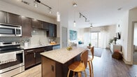 This thoughtfully designed 1-bedroom, 1-bathroom residence offers an efficient and functional single-floor layout with a refined modern aesthetic. The open-concept kitchen and living room serve as the heart of the space, seamlessly connecting the cooking and entertaining areas. The kitchen is outfitted with rich dark espresso cabinetry, a subway tile backsplash, stainless steel appliances — including a refrigerator, range, microwave, and dishwasher — and a granite-topped island with seating for two, ideal for casual dining. Wood-style plank flooring runs throughout the main living area, adding warmth and continuity. The living room is bright and airy, benefiting from natural light that pours in through floor-to-ceiling sliding glass doors leading to a balcony, complemented by a sleek ceiling fan overhead. The bedroom features plush carpeting, generous natural light from a large window, and direct access to the rest of the unit. The bathroom includes a soaking tub with shower and tile flooring, with an adjoining walk-in closet providing ample storage. Additional highlights include multiple closets, a pantry, a dedicated laundry area, and a utility room, ensuring practical storage and convenience throughout.