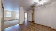 This well-organized 2-bedroom, 1-bathroom residence offers a practical single-floor layout designed for efficient use of space. The main living area features warm hardwood-style flooring and is equipped with a ceiling fan, along with a ceiling-mounted HVAC vent, ensuring year-round comfort. Natural light filters through multiple windows framed with wood trim, lending a bright and welcoming atmosphere throughout.

The kitchen is efficiently arranged in a galley-style configuration, outfitted with light wood cabinetry, laminate countertops, a double sink, a dishwasher, and a full-size refrigerator — all set on durable wood-look flooring.

Both bedrooms are carpeted for comfort and feature baseboard heating units beneath their windows, which offer pleasant views of surrounding greenery. The spacious primary bedroom includes a generous closet with built-in wire shelving and hanging rods. The second bedroom is more intimate in scale but equally well-appointed with natural light.

The bathroom includes a full soaking tub with a shower, a vanity with a wood-toned cabinet, and wood-look tile flooring. A hallway connects all rooms, providing a logical and accessible flow throughout the residence. Clean neutral walls and consistent warm-toned trim unify the overall aesthetic.