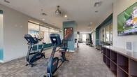 Located at 20050 N Cave Creek Rd in Phoenix, AZ, this expansive single-floor fitness center offers a comprehensive workout environment designed to support a wide range of exercise routines. The space is thoughtfully organized into distinct functional zones across its generous footprint, with patterned carpet tiles throughout the main training areas and a polished hardwood floor in the dedicated studio room.

The main floor features a robust cardio section equipped with stationary bikes, treadmills, and elliptical machines. Strength training is well-represented with a cable machine, Smith machine, bench press station, free weights, and a full dumbbell rack. Mirrored walls in multiple areas enhance the sense of space while aiding form during workouts. The studio room stands out with its hardwood flooring, full-length mirrors, and an assortment of stability balls, medicine balls, and kettlebells organized on a TAG rack — ideal for group fitness or functional training sessions.

The design incorporates teal accent walls that contrast cleanly with light gray and white tones, giving the space a modern, energetic aesthetic. Large windows and glass garage-style doors allow ample natural light to filter in, while recessed lighting and pendant-style ceiling fans ensure the environment remains well-lit and comfortable. Motivational fitness artwork adds character throughout the space.