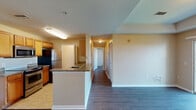 This single-story residence offers a well-organized layout connecting the kitchen, living areas, bedrooms, and bathrooms in a functional flow. The galley-style kitchen is equipped with warm honey-toned cabinetry, granite countertops, stainless steel appliances including a refrigerator, electric range, microwave, and dishwasher, along with a double basin sink. Light tile flooring runs throughout the kitchen, which opens via a peninsula breakfast bar to the adjacent living and dining areas. The living space features dark hardwood-style flooring, a tray ceiling detail, and a sliding glass door providing access to a private balcony with outdoor views. A central hallway connects two well-proportioned bedrooms, each featuring the same dark hardwood-style flooring and windows with exterior views that allow natural light to fill the rooms. Both bathrooms are similarly appointed, featuring granite-topped wood vanities, large mirrors, tile flooring, and a full tub-shower combination. The textured ceilings, neutral warm-toned walls, and consistent finishes throughout contribute to a cohesive and comfortable overall ambiance.