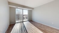 Located at 650 Aguirre Street in Saint Paul, MN, this one-bedroom, one-bathroom unit offers a well-designed layout across a single floor. The open-concept kitchen and living area serves as the heart of the unit, featuring rich dark-walnut cabinetry extending to the ceiling, a large center island with a white quartz countertop and pendant lighting overhead, stainless steel appliances, and light hardwood flooring throughout. Sliding glass doors lead from the living area to a private balcony, flooding the space with natural light and offering outdoor views of the surrounding neighborhood. The bedroom is a comfortable, well-proportioned room finished with plush carpeting and a large window that brings in ample daylight. A dedicated closet provides organized storage, and the bathroom features wood-look tile flooring and a tub-shower combination. Additional practical amenities include an in-unit laundry area and a utility room. Neutral gray tones on the walls complement the warm wood finishes, creating a clean, modern aesthetic throughout. The overall ambiance is bright, functional, and contemporary, making efficient use of the available space.