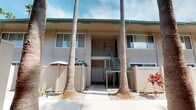 Located at 3131 Cauby Street in San Diego, this single-story building showcases a classic Southern California architectural style with a stucco exterior finished in neutral tones and accented by green-trimmed railings and roofline detailing. The structure is arranged around a central courtyard corridor, where a wide, well-maintained concrete walkway runs between the building facades, creating an inviting pedestrian pathway throughout the property.

Tall, mature palm trees are a defining feature of the exterior, rising prominently along the walkway and lending a distinctly tropical, sun-soaked ambiance characteristic of the San Diego region. Ground-level landscaping incorporates decorative gravel, drought-tolerant plantings, and vibrant accent plants such as red bromeliads, contributing to a low-maintenance yet visually appealing environment.

The building features outdoor metal staircases with sage-green railings providing access between levels, complemented by modern wall-mounted light fixtures. Privacy fencing with a horizontal slat design lines portions of the walkway, adding a contemporary touch while maintaining an open feel. The overall atmosphere is bright and airy, benefiting from abundant natural sunlight and the relaxed, resort-like character typical of well-kept San Diego residential buildings.
