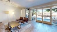 Located at 521 Del Medio Ave within the Palo Alto Plaza in Mountain View, CA, this polished single-floor commercial suite offers a thoughtfully designed layout comprising a living room, dining room, and connecting hallway. Throughout the space, light hardwood flooring and crisp white walls with elegant crown molding create a clean, professional aesthetic.

The living room is a welcoming area featuring a mix of leather and upholstered seating arranged around a sleek coffee table, complemented by framed artwork on the walls. Track lighting and floor lamps provide warm, layered illumination, while large glass doors flood the room with natural light and offer views of the surrounding outdoor area. A private phone booth pod adds a modern, functional touch for focused work or calls.

The dining room serves as an impressive meeting space, anchored by a substantial live-edge wood conference table surrounded by upholstered chairs. A statement pendant light hangs overhead, and recessed lighting enhances the room's refined atmosphere. Curated wall art adds character to the neutral surroundings.

The hallway connects the spaces efficiently, finished with the same hardwood flooring and crown molding details. The suite's consistent design language — neutral tones, quality materials, and modern furnishings — makes it a versatile and professional environment well-suited for business use.