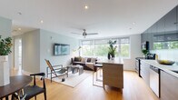 This thoughtfully designed single-floor residence combines modern aesthetics with functional living. The open-concept living and dining area serves as the heart of the home, featuring light hardwood flooring, soft sage-tinted walls, and a wall-mounted flat-screen TV. A ceiling fan complements the recessed lighting, while expansive windows frame lush treetop views, flooding the space with natural light. A round dining table with mid-century modern chairs sits near a convenient in-unit stacked washer and dryer.

The kitchen is sleek and efficient, outfitted with dark upper cabinetry, stainless steel appliances including a range with microwave, light countertops, and a clean subway tile backsplash. A window above the counter brings in additional natural light.

The bedroom is a calm retreat, distinguished by a bold teal accent wall, warm wood-toned headboard, and large windows with treetop views. A ceiling fan, built-in closet with mirrored sliding doors, and curated artwork complete the space.

The bathroom is finished in neutral tones with large-format floor tiles, two-tone wall tiling, a wood-grain vanity with an undermount sink, and a full soaking tub with shower. The overall ambiance is clean, contemporary, and inviting throughout.