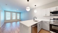 This well-designed 1-bedroom, 1-bathroom unit offers a thoughtful layout across a single floor, combining modern aesthetics with practical functionality. The open-concept living and kitchen area forms the heart of the unit, finished with warm hardwood-style flooring that extends throughout the main living spaces. The kitchen is a standout feature, equipped with stainless steel appliances including a range, microwave, dishwasher, and refrigerator. Two-tone cabinetry pairs white upper cabinets with grey lower cabinets, complemented by crisp white countertops and a peninsula island with a built-in sink. Stylish globe pendant lights add a contemporary touch overhead. The living area benefits from multiple windows that invite natural light and connect seamlessly to the kitchen. The spacious primary bedroom features soft carpeting, generous wall space, and a window that brings in additional natural light. A dedicated closet provides convenient storage. The bathroom is finished with wood-style flooring, a full tub-shower combination, and matte black fixtures that lend a modern, cohesive look. Neutral grey-toned walls throughout the unit create a clean, versatile backdrop suited to a variety of interior styles.