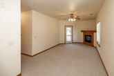 This 2-bedroom, 1-bathroom single-floor unit offers a comfortable and functional layout with warm, neutral finishes throughout. The living area serves as the heart of the space, featuring plush carpeting, a ceiling fan with light fixture, and a wood-trimmed fireplace that adds a cozy focal point. Natural light filters in through multiple windows, and a sliding glass door provides access to an outdoor area. The transition between the living space and kitchen is marked by a shift to light hardwood-style flooring. The galley-style kitchen is efficiently designed with ample light wood cabinetry, white countertops, and a full suite of white appliances including a refrigerator, electric range, microwave, and dishwasher. Both bedrooms are carpeted and generously proportioned, with the primary bedroom featuring mirrored sliding closet doors and a ceiling fan, while the second bedroom benefits from large windows that invite natural light and outdoor views. The bathroom is finished with warm tile flooring and includes a full soaking tub with a shower rod. Warm oak-toned baseboards and door trim carry consistently throughout the unit, lending a cohesive and inviting character to the entire space.
