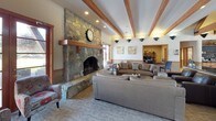 Located at 2711 East Adirondack Lane in Spokane, WA, this single-floor facility offers a thoughtfully designed layout that blends communal gathering spaces with functional everyday amenities. The dramatic entry lobby sets the tone immediately, featuring soaring exposed timber beams, a vaulted ceiling, large French doors, and natural stone tile flooring that creates a warm and welcoming first impression. Adjacent to the entry is an interior coffee and refreshment station, complete with wood cabinetry, open shelving, and a chalkboard menu wall beneath the same striking beam ceiling. The open living and dining area is anchored by rich hardwood-style flooring, recessed lighting, and wood-trimmed windows that invite abundant natural light. A built-in wood bookcase with integrated media center serves as a central focal point in the living space. The well-appointed kitchen features warm wood cabinetry, a stone tile backsplash, light countertops, stainless appliances, and a central island with bar seating. A separate dining room accommodates a full-size table and benefits from multiple windows with views of the surrounding greenery. Additional rooms include a carpeted activity or game room with a wall-mounted television, and a quiet flex room with natural light and neutral finishes throughout. The space balances comfort, functionality, and community-oriented design.
