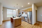 Located at 3401 E Washington Ave in Madison, WI, this well-appointed 2-bedroom, 2-bathroom residence offers a thoughtfully designed single-level layout that balances comfort and functionality. The open-concept kitchen and living area serves as the heart of the home, featuring warm wood-toned cabinetry, granite countertops, a tile backsplash, and a full suite of stainless steel appliances including a range, microwave, dishwasher, and refrigerator. A central island with elegant pendant lighting provides additional workspace and casual dining space, while a ceiling fan and large windows in the living area fill the space with natural light and outdoor views. Durable hardwood-style flooring runs throughout the main living areas, complemented by plush carpet in the bedrooms. The primary bedroom is a comfortable retreat, while the second bedroom benefits from a large window overlooking the surrounding landscape. Both bathrooms are finished with granite vanities and hardwood-style flooring, with one bathroom featuring accessibility grab bars for added convenience. A dedicated in-unit laundry room houses a full-size front-loading washer and dryer with built-in shelving above. A closet and well-placed hallways complete this practical, modern layout.