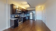 Located at 300 Seven Springs Way in Nashville, TN, this single-floor unit offers a well-designed layout with modern finishes throughout. The kitchen is a standout feature, showcasing rich dark cabinetry, granite countertops, a blue-gray subway tile backsplash, and a full suite of stainless steel appliances including a refrigerator, dishwasher, electric range, and built-in microwave. Hardwood-style flooring runs throughout the main living and kitchen areas, adding warmth and continuity to the space. The open living area benefits from abundant natural light, enhanced by French doors that open to a private balcony, offering outdoor views of the surrounding neighborhood. A ceiling fan with track lighting overhead completes the living space with both style and function. The bedroom is carpeted for comfort and features a large window that frames greenery outside, along with a ceiling fan to maintain airflow. The bathroom is finished with granite countertops, dark cabinetry, and a well-lit mirror, directly adjoining a spacious walk-in closet equipped with built-in shelving and hanging racks. The overall ambiance is clean, contemporary, and move-in ready, reflecting a cohesive design aesthetic throughout.