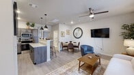 This thoughtfully designed one-bedroom, one-bathroom unit in Amarillo, Texas offers a cohesive and functional layout across a single floor. The kitchen is a standout feature, showcasing gray shaker-style cabinetry with matte black hardware, granite countertops, stainless steel appliances including a range, microwave, and dishwasher, and light wood-style flooring that extends into the adjoining living and dining areas. A breakfast bar with pendant lighting adds both functionality and style to the space. The open living and dining area is bright and welcoming, with a large window dressed in light curtains that allows natural light to fill the room. A decorative wall-mounted mirror and TV nook complement the dining setup, while the living area offers a relaxed, comfortable atmosphere. The bedroom is a serene retreat, featuring plush carpeting, a ceiling fan, a generous window with blinds and curtains, and ample room for a full furniture arrangement. The bathroom continues the cohesive design aesthetic with matching gray cabinetry, granite countertops, a framed mirror, and modern vanity lighting. Clean tile flooring and upper storage cabinets complete the space with both form and function.