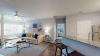 This single-floor, two-bedroom, two-bathroom residence offers a thoughtfully designed layout with a cohesive color palette of soft grays and crisp whites throughout. The open-concept living and dining areas are unified by rich, dark hardwood flooring and elegant crown molding. The living room centers around a tiled fireplace flanked by a wall-mounted television, creating a comfortable gathering space. Adjacent to it, the dining area benefits from a geometric chandelier overhead and direct access to the granite-topped breakfast bar that seamlessly connects to the kitchen.

The kitchen is well-equipped with white shaker cabinetry, granite countertops, a subway tile backsplash, and stainless steel appliances, offering both style and functionality. Both bedrooms feature plush carpeting, ample natural light from large windows with curtains, and ceiling fans. The primary bedroom includes a private en-suite bathroom, while the second bathroom features a tub-shower combination with white tile surround and granite-topped vanity. Consistent dark hardwood flooring in the bathrooms ties the overall design together, lending the residence a polished, unified aesthetic.