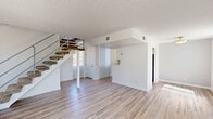 Located at 449 East Arenas Road in Palm Springs, California, this two-story, two-bedroom, one-bathroom home offers a clean, modern aesthetic with a practical and efficient layout spread across two floors. The main level hosts a bright, open-concept living, dining, and kitchen area finished with light wood-look flooring and crisp white walls. A carpeted staircase with a metal railing connects the two floors, adding a functional architectural element to the space. The kitchen features two-tone cabinetry with warm walnut lower cabinets and white uppers, white countertops, stainless steel appliances including a refrigerator and dishwasher, and a coil cooktop range. A pass-through counter connects the kitchen to the main living area, enhancing the open feel. Natural light filters in through vertical blind-covered windows throughout. The upper floor contains both bedrooms, each carpeted and fitted with closets featuring mirrored sliding doors. The bedrooms receive ample natural light through large windows with vertical blinds. The shared full bathroom features wood-look tile flooring, a single vanity with warm wood cabinetry, a wall-mounted mirror, and a tub-shower combination. A utility room and hallway complete the floor plan, providing practical storage and circulation space.