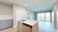 Located on State Line Road in Kansas City, KS, this well-appointed 2-bedroom, 2-bathroom unit offers a thoughtfully designed single-floor layout. The open-concept kitchen and living area serves as the heart of the home, featuring a central island with a stainless steel sink and dishwasher, sleek gray cabinetry, white subway tile backsplash, and a full suite of stainless steel appliances including a refrigerator, microwave, and range. Light wood-style flooring flows throughout the main living areas, complementing the neutral gray and white color palette. The spacious living room is bathed in natural light through full-height sliding glass doors fitted with vertical blinds, opening to an outdoor view. Both bedrooms are carpeted and feature multiple windows that bring in additional natural light, creating a warm and comfortable atmosphere. Each bedroom is paired with its own closet, including a walk-in closet with wire shelving systems for organized storage. The bathrooms are clean and functional, with one featuring a full soaking tub and shower combo with built-in shelving. Recessed lighting throughout and a modern, minimalist aesthetic give the entire space a fresh, contemporary feel.