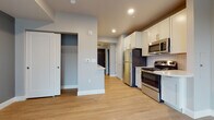 This well-appointed single-floor unit offers a clean, modern aesthetic carried consistently throughout each space. Light hardwood flooring runs throughout, complementing the soft neutral and blue-gray wall tones that give the unit a calm, cohesive feel.

The kitchen is thoughtfully designed with white shaker-style cabinetry extending to the ceiling, providing generous storage. A herringbone-patterned tile backsplash adds a subtle decorative touch behind the stainless steel gas range, over-the-range microwave, and refrigerator. A compact peninsula with a light countertop serves as a natural divider between the kitchen and the adjacent living area. Recessed lighting keeps the kitchen bright and functional.

The living area is open and airy, highlighted by a large sliding glass door that fills the space with natural light and opens onto a private balcony with views of the surrounding neighborhood. A large closet with wire shelving is conveniently located within the main living area, offering practical everyday storage.

The bathroom is finished in a clean, contemporary style featuring a full soaking tub with a subway-tiled surround, a white vanity with a modern countertop, brushed nickel hardware, and a large mirror that enhances the sense of space.

Overall, the unit presents a fresh, move-in-ready interior with a well-balanced layout and modern finishes throughout.