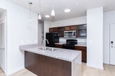 Located at 1235 E Wilmington Ave in Salt Lake City, UT, this 2-bedroom, 2-bathroom residence offers a well-organized, single-floor layout designed for comfortable living. The open-concept kitchen and living area forms the heart of the home, anchored by a prominent peninsula with granite countertops, a double stainless steel sink, and warm-toned wood cabinetry. Pendant lighting illuminates the peninsula, while the kitchen is equipped with stainless steel appliances, including a microwave and electric range. Light hardwood flooring extends throughout the main living areas, enhancing the bright, airy atmosphere. The living room opens to a large sliding glass door with vertical blinds, inviting ample natural light. The spacious primary bedroom features plush carpeting and a dedicated closet area, while the second bedroom also offers carpeted flooring and a window with exterior views. Both bathrooms are consistently finished with granite-topped vanities, rich wood cabinetry, full tub-shower combinations, and light wood flooring. A connecting hallway ties the rooms together efficiently. Textured ceilings and neutral wall tones throughout contribute to a clean, cohesive aesthetic suited for a range of living styles.