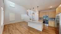 Located at 6519 Kings Glen Drive in Humble, TX, this two-story home offers a well-designed layout across two floors. The main level features an open-concept kitchen and living area with soaring ceilings that create an airy, expansive feel. The kitchen is outfitted with light wood cabinetry, granite countertops, a large center island with an undermount sink, stainless steel appliances, and stylish pendant lighting. Warm hardwood-style flooring flows seamlessly throughout both levels, complementing the home's clean, contemporary aesthetic. Multiple windows dressed with white blinds allow generous natural light into every room. The upper floor houses the majority of the five bedrooms, including a spacious primary suite with its own walk-in closet featuring built-in shelving and a private ensuite bathroom. The ensuite includes a tiled walk-in shower, granite vanity, and warm wood cabinetry. Additional bathrooms maintain the same modern finishes, including granite countertops and wood-toned storage cabinets. The secondary bedrooms are well-proportioned, each with windows providing natural light. Three closets, two hallways, and multiple staircases contribute to practical circulation throughout the home. The overall design emphasizes clean lines, neutral tones, and functional spaces suitable for a variety of living arrangements.