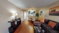 This single-story, one-bedroom, one-bathroom unit is thoughtfully designed to maximize its footprint through an open, flowing layout. The main living area features warm hardwood-style flooring that extends throughout, creating a cohesive and inviting atmosphere. A ceiling fan overhead and a large sliding glass door leading to a private patio fill the space with natural light, while vertical blinds provide adjustable privacy. The living room comfortably accommodates a full sectional seating arrangement alongside a media console, demonstrating the practical use of the space.

The dining area connects seamlessly to the kitchen, which is accessible via a breakfast bar pass-through. The kitchen itself is galley-style, outfitted with dark espresso cabinetry, light countertops, stainless steel appliances including a refrigerator, electric range, and over-the-range microwave, as well as a double sink. Hardwood-style flooring continues in this area, complemented by overhead lighting.

The bedroom offers a quieter retreat with plush wall-to-wall carpeting, a textured ceiling, and a window with blinds that provides natural light. The neutral wall tones throughout the unit contribute to a calm, versatile ambiance suited to a variety of décor styles.