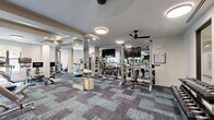 Located at 1900 Yorktown St in Houston, Texas, this fitness center offers a generously sized, single-floor exercise space designed to support a comprehensive workout experience. The room features a distinctive patterned carpet in muted blue and gray tones, lending the space a modern, polished aesthetic that sets it apart from typical gym environments.

Floor-to-ceiling mirror panels are strategically positioned throughout the room, creating a sense of expansiveness while allowing users to monitor their form during exercise. The mirrors also reflect the abundant lighting provided by flush-mount circular ceiling fixtures and recessed lighting, keeping the space bright and energizing. Ceiling fans add to the comfort of the environment.

The fitness center is well-stocked with a wide variety of equipment. The cardio section includes multiple treadmills and stationary bikes, each equipped with individual monitors. The strength training area features cable machines, a multi-station weight apparatus, a dedicated free weights rack with dumbbells, kettlebells, and medicine balls in an array of sizes, as well as a flat workout bench. Wall-mounted flat-screen televisions are positioned throughout the space for entertainment.

Natural light filters in through windows along one wall, offering a pleasant connection to the outdoors. The layout is thoughtfully arranged into distinct zones, ensuring ample circulation space between equipment for a safe and comfortable workout experience.