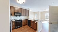 This 1-bedroom, 1-bathroom unit delivers a well-organized single-floor layout that maximizes every square foot. The open-concept kitchen is a standout feature, showcasing rich walnut-toned shaker cabinetry, granite countertops, a peninsula with an undermount sink, and a full suite of black appliances including a range, microwave, dishwasher, and refrigerator. Hardwood-style flooring runs throughout the kitchen and flows seamlessly into the living room, which is bathed in natural light through large windows. A ceiling fan adds comfort to the airy living space. Neutral, warm-toned walls create a cohesive and inviting atmosphere throughout. The bedroom is carpeted for added comfort and features direct access to a dedicated walk-in closet with built-in shelving and hanging rods. The full bathroom is finished with light tile flooring, a tub-shower combination with white tile surround, a granite-topped vanity with wood cabinetry, and brushed nickel fixtures. The overall design blends practical functionality with clean, modern finishes, making this a comfortable and efficient living space.