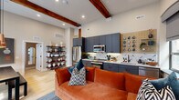 This thoughtfully designed 3-bedroom, 2-bathroom single-floor residence blends industrial character with modern comfort. The open-concept living and kitchen area is the heart of the home, anchored by soaring ceilings adorned with striking exposed wood beams that lend warmth and architectural interest. The kitchen is well-appointed with slate-gray cabinetry, stainless steel appliances, a bold herringbone tile backsplash, and light quartz countertops, all set atop light hardwood flooring that runs throughout the space. The living area benefits from generous natural light through multiple windows and features an inviting layout with vibrant design touches. The three bedrooms each carry a distinct personality — one features rich terracotta walls with a closet and window, while another offers a more subdued, earthy green palette with outdoor views. The primary bedroom is a comfortable retreat with thoughtful proportions. The two bathrooms are clean and contemporary, with one showcasing large-format tile flooring, a floating wood vanity, and a fully tiled walk-in shower. A hallway with decorative wall-mounted accents and a structural wood column adds further character. This space masterfully balances bold design choices with functional, well-organized living.