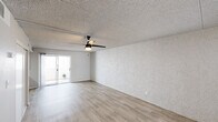 This single-floor unit is thoughtfully laid out to maximize its compact footprint, incorporating a living room, kitchen, bathroom, and closet within an efficient floor plan. Light wood-style flooring runs throughout the space, creating visual continuity and a clean, cohesive aesthetic.

The living area is open and unobstructed, featuring textured stucco-style walls, a popcorn ceiling, and a ceiling fan with integrated lighting. A sliding glass door allows natural light to fill the room while providing access to an outdoor area. A window near the entry further brightens the space.

The kitchen is well-appointed for its size, featuring white shaker-style cabinetry, subway tile backsplash, and a full suite of stainless steel appliances including a refrigerator, electric range, over-the-range microwave, and a stainless steel sink. The layout makes efficient use of available counter and storage space.

The bathroom includes a wood-toned vanity with a white countertop, a large mirror with overhead lighting, and a towel bar. A dedicated closet accessible from the bathroom provides organized storage with built-in shelving and a hanging rod. The overall ambiance of the unit is bright, clean, and functional.