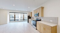 Located at 101 N Broadway Ave in downtown Oklahoma City, this well-appointed one-bedroom, one-bathroom unit offers a thoughtfully designed open-concept layout. The combined living, dining, and kitchen area is anchored by expansive floor-to-ceiling windows that flood the space with natural light and offer views of the surrounding urban streetscape. The kitchen features light natural wood cabinetry with brushed gold hardware, light-toned countertops, a subway tile backsplash, a gold-accented sink, and a full suite of stainless steel appliances. Terrazzo-style flooring runs consistently throughout, lending a clean, contemporary aesthetic to the entire unit. The bedroom is a comfortable, well-proportioned room with a ceiling fan, double closet doors with gold hardware, and crisp white walls. A second closet provides additional storage. The bathroom is finished with classic white hexagon tile flooring with decorative dark accents, marble-style tiled surround in the tub/shower, gold fixtures, a wood vanity, and a dark stone countertop. An in-unit laundry closet with a stacked washer and dryer adds everyday convenience. Recessed lighting throughout completes this bright, modern urban residence.