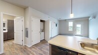 This well-appointed single-floor unit offers a thoughtfully designed open-concept layout that seamlessly connects the kitchen and living area. The kitchen is a standout feature, showcasing rich dark-toned cabinetry, white countertops, a peninsula with an undermount sink and pendant lighting above, and a full suite of black appliances including a refrigerator, range, and built-in microwave. Wood-look vinyl plank flooring runs throughout the main living areas, adding warmth and durability. The living space is bright and airy, with a wall-mounted mini-split system for climate control, a glass-panel exterior door, and large windows that invite ample natural light. A dedicated hallway leads to the bedrooms and utility areas. The bedrooms feature plush carpeting, baseboard heating, additional mini-split units, and windows with outdoor views. A spacious bathroom includes a wide vanity with dark cabinetry, a linen tower, a large mirror with vanity lighting, and easy-care flooring. In-unit laundry is conveniently housed in a dedicated closet. The neutral color palette and clean, modern finishes throughout create a cohesive and comfortable living environment.