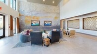 Located in Richmond, Virginia, this single-floor community clubhouse delivers a refined blend of contemporary design and thoughtful craftsmanship. The centerpiece of the space is a soaring double-height lounge area bathed in natural light through floor-to-ceiling windows, offering direct views of the outdoor pool area. A sweeping large-scale abstract mural anchors one wall, flanked by dual wall-mounted televisions, while plush curved sofas and sculptural lounge chairs create an inviting social atmosphere. Distinctive architectural accents are found throughout, including decorative latticed wall panels framed in warm wood set against geometric patterned tile flooring, adding artful texture to transitional areas. The kitchen features rich walnut cabinetry, dark stone countertops, and stainless steel appliances, complemented by a sculptural 3D white tile backsplash and sleek pendant lighting. A marble-clad feature wall with gold veining adds a luxurious focal point near the bar seating area, where a polished stone countertop and leather chairs invite casual gatherings. Recessed lighting and pendant fixtures provide warm illumination throughout, while the cohesive palette of natural stone, warm wood tones, and neutral walls creates a sophisticated and welcoming environment.