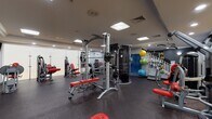Located at 150 Southfield Ave in Stamford, Connecticut, this two-floor fitness center offers a comprehensive and thoughtfully organized workout facility. The main floor is expansive, housing a robust selection of Matrix-brand cardio equipment, including a long row of treadmills, upright and recumbent stationary bikes, and elliptical machines, all positioned beneath bright overhead lighting. Large mirrored walls enhance the sense of space and allow users to monitor their form throughout their workouts. A glass-partitioned area on this level appears to serve as a dedicated court space, adding versatility to the facility. The upper level, accessed via a staircase visible in the floor plan, features strength training equipment, including cable machines, weight benches with red upholstery, and a variety of resistance machines. Colorful stability balls and stacked exercise mats are neatly organized along the walls. A rack of color-coded dumbbells provides options for free weight training. Wall-mounted televisions offer entertainment, while private rooms with white doors provide additional amenities. Throughout both floors, durable rubber flooring ensures safety and comfort. The overall ambiance is clean, modern, and well-maintained, making it a fully functional facility suited for a wide range of fitness goals.