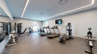 Located at 2416 Scranton Rd in Cleveland's vibrant Ohio City neighborhood, this fitness center offers a thoughtfully designed, single-floor space built to support a comprehensive workout experience. The facility is divided into distinct functional zones, each outfitted with quality equipment to accommodate a variety of training styles.

The main cardio area features multiple treadmills, an elliptical trainer, stationary bikes, and a rowing machine, all arranged to maximize open floor space. Durable rubber flooring throughout provides traction and impact absorption. A wall-mounted flat-screen television adds an entertainment option for cardio sessions. Recessed linear LED lighting runs along the tray ceiling perimeter, creating a clean, modern ambiance with even illumination across the space.

A dedicated strength training section includes a multi-station cable machine, an adjustable weight bench, and a full dumbbell rack accompanied by kettlebells, offering a well-rounded free weights area. A large wall mirror in this section enhances the sense of space and supports proper form during workouts.

A separate adjoining room provides a quieter area for stretching or floor exercises, equipped with a wall-mounted mat holder and additional cardio equipment. Natural light enters through multiple windows, contributing to an open and energizing atmosphere throughout the facility.