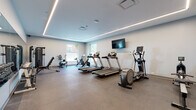 Located at 2416 Scranton Rd in Cleveland's vibrant Ohio City neighborhood, this fitness center offers a thoughtfully designed, single-floor space built to support a comprehensive workout experience. The facility is divided into distinct functional zones, each outfitted with quality equipment to accommodate a variety of training styles.

The main cardio area features multiple treadmills, an elliptical trainer, stationary bikes, and a rowing machine, all arranged to maximize open floor space. Durable rubber flooring throughout provides traction and impact absorption. A wall-mounted flat-screen television adds an entertainment option for cardio sessions. Recessed linear LED lighting runs along the tray ceiling perimeter, creating a clean, modern ambiance with even illumination across the space.

A dedicated strength training section includes a multi-station cable machine, an adjustable weight bench, and a full dumbbell rack accompanied by kettlebells, offering a well-rounded free weights area. A large wall mirror in this section enhances the sense of space and supports proper form during workouts.

A separate adjoining room provides a quieter area for stretching or floor exercises, equipped with a wall-mounted mat holder and additional cardio equipment. Natural light enters through multiple windows, contributing to an open and energizing atmosphere throughout the facility.