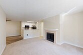 Located in Lynnwood, Washington, this two-bedroom, two-bathroom residence offers a well-organized single-floor layout designed for comfortable everyday living. The open living room is a standout space, featuring plush carpeting, a tile-surround fireplace with a classic white mantel, and a sliding glass door that opens to a private balcony with views of surrounding greenery. The kitchen is efficiently designed with white cabinetry, light marble-style countertops, black appliances including a range and refrigerator, and durable wood-look vinyl flooring that extends through the entry and kitchen areas. A breakfast bar peninsula connects the kitchen to the living space, enhancing the open flow. Both bedrooms are carpeted and finished in soft, neutral tones, each offering closet storage. The primary bedroom is generously sized with ample room for furnishings. The two bathrooms feature wood-look tile flooring, white vanities with updated hardware, and tub-shower combinations. A dedicated in-unit laundry area accommodates a full-size washer and dryer with overhead wire shelving for added storage. Throughout the residence, a consistent palette of warm whites and beiges creates a clean, cohesive ambiance.