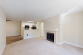 Located in Lynnwood, Washington, this two-bedroom, two-bathroom residence offers a well-organized single-floor layout designed for comfortable everyday living. The open living room is a standout space, featuring plush carpeting, a tile-surround fireplace with a classic white mantel, and a sliding glass door that opens to a private balcony with views of surrounding greenery. The kitchen is efficiently designed with white cabinetry, light marble-style countertops, black appliances including a range and refrigerator, and durable wood-look vinyl flooring that extends through the entry and kitchen areas. A breakfast bar peninsula connects the kitchen to the living space, enhancing the open flow. Both bedrooms are carpeted and finished in soft, neutral tones, each offering closet storage. The primary bedroom is generously sized with ample room for furnishings. The two bathrooms feature wood-look tile flooring, white vanities with updated hardware, and tub-shower combinations. A dedicated in-unit laundry area accommodates a full-size washer and dryer with overhead wire shelving for added storage. Throughout the residence, a consistent palette of warm whites and beiges creates a clean, cohesive ambiance.