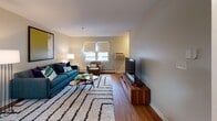 Located in Boston's Mission Hill neighborhood, this two-floor residence at 28 St Alphonsus Street offers a well-organized layout with hardwood flooring throughout and a warm, neutral color palette that creates a cohesive feel across all rooms.

The main level features a living room with natural light from street-facing windows, providing views of the surrounding neighborhood. The space accommodates a comfortable seating arrangement and flows into a dedicated dining area highlighted by a pendant light fixture. The kitchen is outfitted with warm honey-toned wood cabinetry, ample counter space, and white appliances including a range, dishwasher, and refrigerator, with a window above the sink offering additional natural light.

Also on this level is a flexible room with large windows framing views of autumn foliage, well-suited as a home office or secondary sitting area. A full bathroom features a tub-shower combination, a wood-framed vanity, and matching flooring.

The upper level houses the bedrooms, each with hardwood floors, closet storage, and windows providing outside views. The primary bedroom is generously sized with a wide closet. A staircase with a dark runner connects both floors, contributing to the home's functional and comfortable layout throughout.