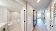 Located on the 17th floor of a high-rise in Arlington, Virginia, this contemporary unit offers a well-designed, single-level layout with modern finishes throughout. Light wood-style flooring flows across the main living areas, complementing the neutral, warm-toned walls and clean white trim that define the space.

The kitchen is a standout feature, outfitted with soft sage-blue shaker cabinetry accented by matte black hardware, a classic white subway tile backsplash, bright white countertops, and a full suite of stainless steel appliances including a range, over-the-range microwave, and dishwasher. A matte black faucet adds a polished, cohesive touch. Floor-to-ceiling windows adjacent to the kitchen flood the space with natural light and provide direct access to a private balcony with open city views.

The bedroom continues the light, airy aesthetic with the same wood-style flooring, large windows, and a sliding barn-style door with frosted glass panels — a stylish architectural detail that adds both function and character to the hallway.

The bathroom is finished with elegant marble-look tile flooring, sage-toned cabinetry with black hardware, a white countertop vanity, and a fully tiled soaking tub surround. Recessed lighting throughout the unit ensures bright, even illumination in every room.