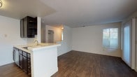 This three-bedroom, two-bathroom single-story residence offers a thoughtfully designed open-concept layout that maximizes both space and functionality. The living and dining area flows seamlessly from the kitchen, creating an inviting, connected environment filled with natural light from multiple windows dressed with blinds. Rich, dark hardwood-style flooring runs consistently throughout the entire unit, adding warmth and visual continuity.

The kitchen is well-appointed with dark espresso cabinetry, a breakfast bar peninsula with sink, stainless steel appliances including a range, microwave, and refrigerator, and a dark tile backsplash that adds a bold contrast to the light countertops.

Each of the three bedrooms features the same hardwood-style flooring, clean white walls, and windows that bring in ample natural light. The bedrooms are generously proportioned, with at least one featuring corner windows for added brightness. Sliding-door closets with built-in shelving and hanging rods provide practical storage solutions.

Both bathrooms are finished with dark vanity cabinetry, light countertops, large mirrors, and full tub-shower combinations with white tile surrounds. Consistent chrome fixtures and hardwood-style flooring tie the bathrooms cohesively to the rest of the home.