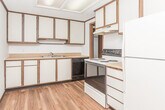 Located at 205–219 E Edgewood Blvd in Lansing, Michigan, this single-floor unit offers a practical and well-organized layout suited for comfortable everyday living. The kitchen is efficiently designed with ample white cabinetry trimmed in warm wood tones, a double-basin sink, laminate wood flooring, a electric coil range, a black dishwasher, and a full-size refrigerator. A range hood and a skylight-style overhead fixture provide both ventilation and bright illumination. The living areas feature neutral-toned carpet, textured ceilings, and dark wood crown molding and baseboards that carry a consistent design theme throughout the unit. One room includes a built-in wall unit with wood-framed shelving and lower cabinet storage, adding both character and functionality, while a ceiling fan provides air circulation. The bedrooms are generously sized, each with carpeted floors, windows dressed with vertical blinds that allow natural light and outdoor views, and ceiling fans in select rooms. The full bathroom includes a marble-topped vanity, hardwood-style flooring, and a full tub-shower combination. A dedicated laundry room with hardwood-style flooring houses an in-unit washer and dryer alongside a water heater, completing this functional and cohesive living space.