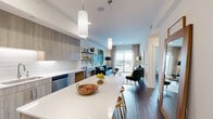 Located at 3120 Smith St in Houston's vibrant Montrose neighborhood, this 1-bedroom, 1-bathroom residence offers a thoughtfully designed open-concept floor plan across a single level. The combined kitchen, dining, and living area serves as the heart of the home, featuring rich dark hardwood-style flooring, contemporary pendant lighting, and a seamless flow toward a private balcony with city views. The kitchen is outfitted with full-height wood-toned cabinetry, a white quartz waterfall island with bar seating, a white subway tile backsplash, and a complete suite of stainless steel appliances. The living area provides generous space for entertaining and opens directly to the balcony. The bedroom is a calm retreat with tall ceilings, a ceiling fan, natural light from large windows, and direct access to the bathroom. The bathroom features light wood vanity cabinetry, a white quartz countertop, an illuminated mirror, and a full soaking tub with shower. A walk-in closet accessed through the bathroom offers organized shelving and hanging storage. Additional highlights include a dedicated laundry area, a second closet, and a welcoming entrance. The overall aesthetic is modern and cohesive, combining neutral tones with warm wood accents throughout.