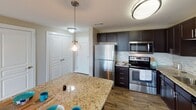 This single-floor residence in Charlotte, NC, offers a thoughtfully designed open layout that connects the kitchen and living areas seamlessly. The kitchen is a standout space, equipped with dark espresso cabinetry, granite countertops, a decorative tile backsplash, stainless steel appliances including a refrigerator, range, microwave, and dishwasher, and a central island with pendant lighting overhead. Wood-look flooring grounds the kitchen, while track lighting illuminates the open living area, which transitions to soft carpeting. Large windows and sliding glass doors flood the living spaces with natural light and provide views of surrounding greenery.

The bedrooms are carpeted and generously sized, each featuring ceiling fans and large windows with vertical blinds that frame outdoor tree views. Both bathrooms are finished with granite-topped dark vanities, large mirrors, and tile flooring. The primary bathroom includes a tub-shower combination with white tile surround, while the secondary bathroom features a shower with a curtain and access to a walk-in closet. The overall aesthetic is clean and contemporary, with a neutral color palette throughout.