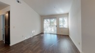 This two-bedroom, one-bathroom unit is designed with a practical and functional layout across a single floor. The open-concept living and dining area features rich wood-style flooring that extends throughout the main living spaces, creating a cohesive and polished look. A sliding glass door floods the living room with abundant natural light and provides direct access to the outdoors, with views of surrounding greenery. An additional window further enhances the bright, airy atmosphere of the space.

The kitchen is outfitted with dark espresso cabinetry, light countertops, and a full suite of appliances including an electric range, over-the-range microwave, refrigerator, and dishwasher. A pendant light fixture adds a finishing touch to the kitchen area, which opens seamlessly to the living space.

Both bedrooms feature soft carpeting and windows with blinds that allow for natural light and privacy. A walk-in closet is visible in one of the bedrooms, offering ample storage.

The bathroom includes a dark-toned vanity with a wide countertop, a large mirror, and a shower/tub combination. A dedicated in-unit laundry closet houses a full-size washer and dryer with built-in shelving above for additional storage. The hallway connecting the rooms provides convenient access to all areas of the unit.