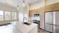 This modern 2-bedroom, 2-bathroom residence in Denver's sought-after 80210 neighborhood offers a thoughtfully designed open-concept floor plan with impressive soaring ceilings that amplify the sense of space throughout. Rich, dark hardwood floors flow through the main living areas, complementing the bright, neutral palette that fills the home with warmth and light.

The kitchen serves as a central hub of the home, featuring a large center island with a white quartz countertop and an undermount sink, warm wood-grain cabinetry, a classic subway tile backsplash, stainless steel appliances, and stylish pendant lighting. The open living and den areas are bathed in natural light from generous windows and offer a seamless connection to the private balcony.

Both bedrooms are carpeted for comfort, with high ceilings and ample closet space — including a spacious walk-in closet with built-in shelving and drawer systems in the primary suite. The two bathrooms are finished with large-format tile flooring, wood-toned vanities, white countertops, and clean modern fixtures. Additional conveniences include in-unit laundry, multiple closets, and hallways that connect the layout efficiently.